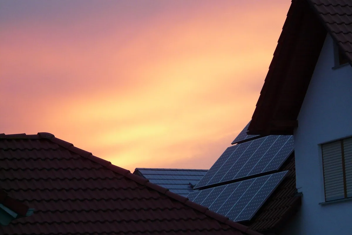 Placas solares en el tejado de una vivienda al atardecer, con el cielo anaranjado