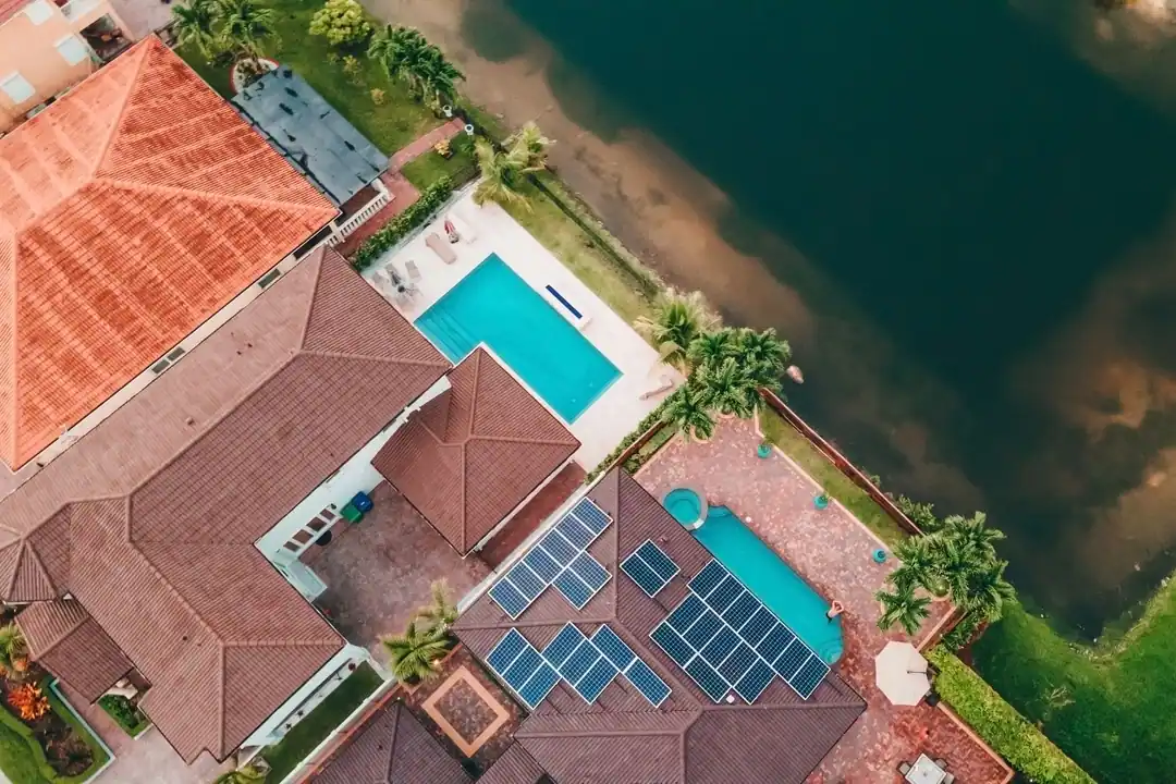 Vista aérea de una casa con piscina y placas solares en el tejado, junto al vaso