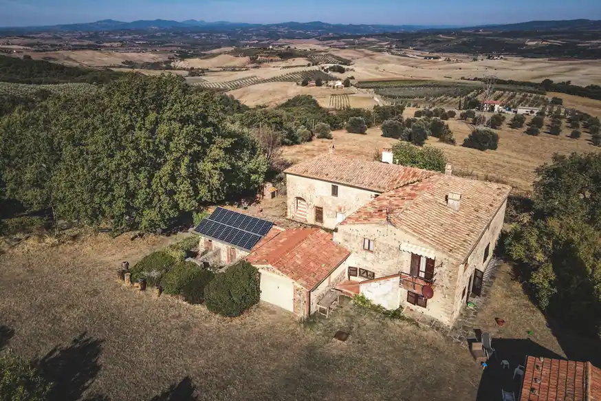 Casa de campo de piedra vista desde el aire, con placas solares sobre el tejado de un anexo, en un paisaje seco de lomas