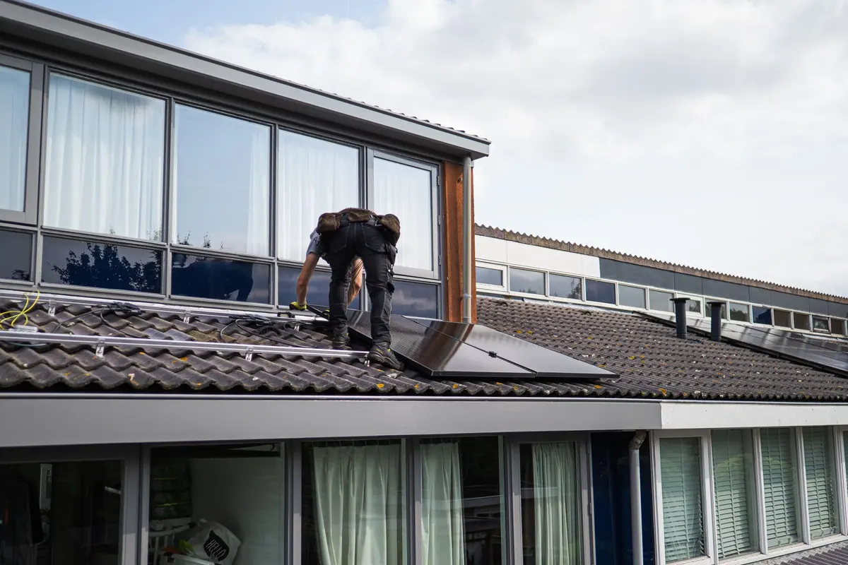 Instalador colocando un panel solar sobre los raíles del tejado de una vivienda