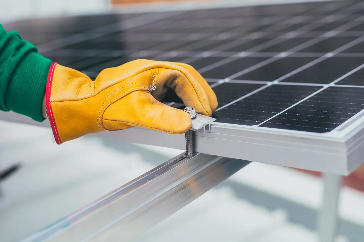 Mano con guante de trabajo apretando el tornillo de la grapa que sujeta una placa solar al perfil de aluminio