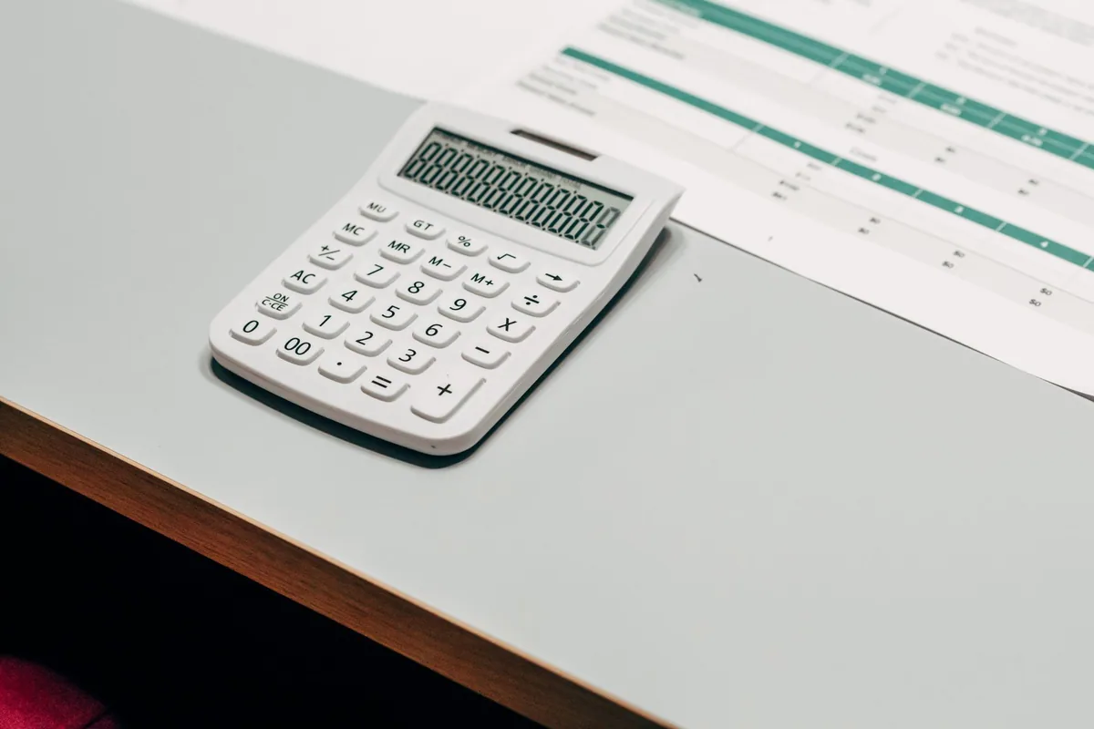 Calculadora blanca sobre una mesa junto a una hoja impresa con una tabla de importes