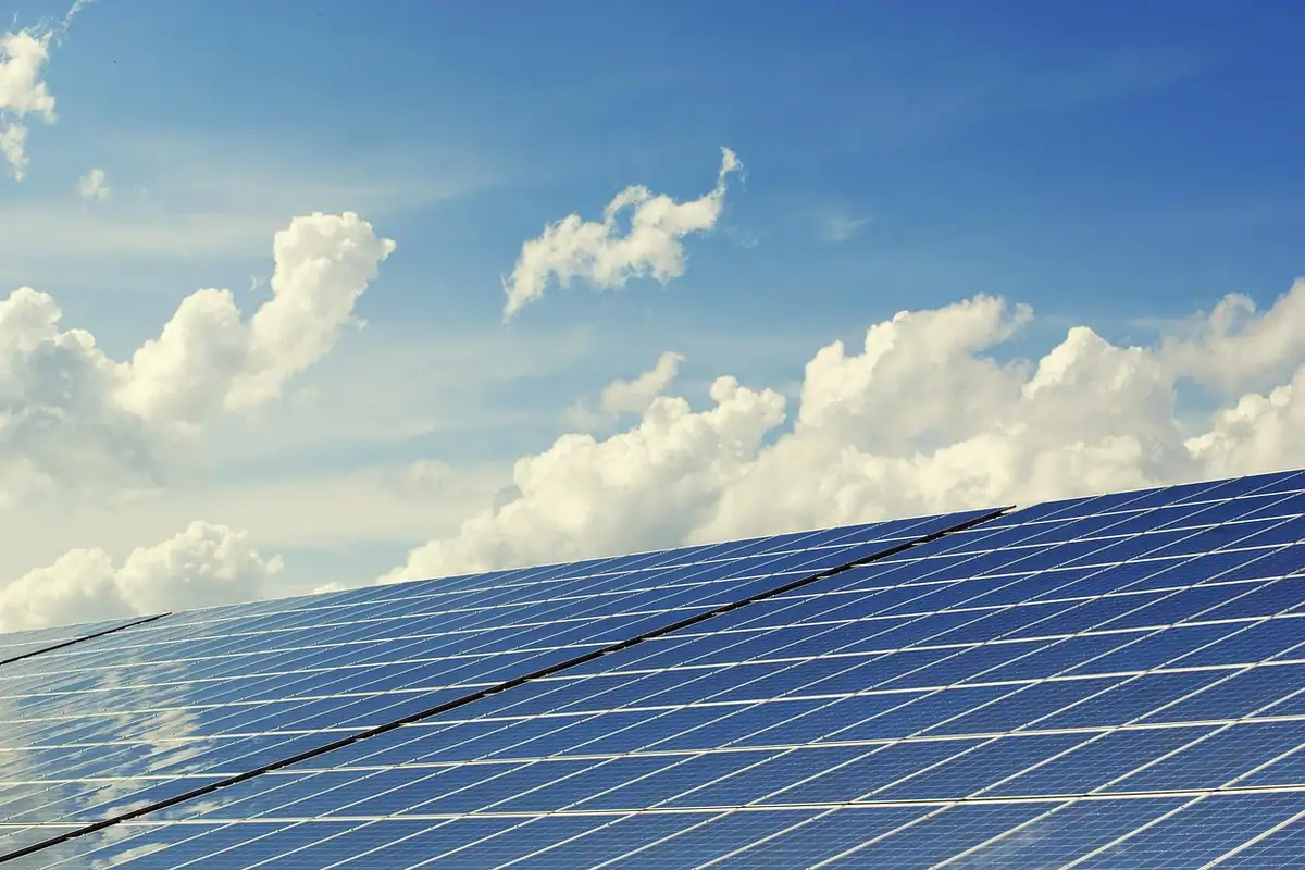 Filas de placas solares a pleno sol bajo un cielo azul con nubes blancas