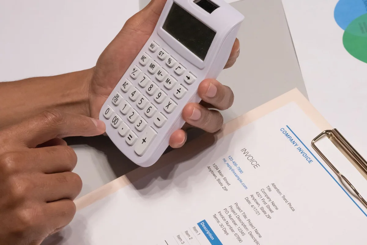 Manos con una calculadora sobre una factura genérica, para estimar cuántas placas solares hacen falta